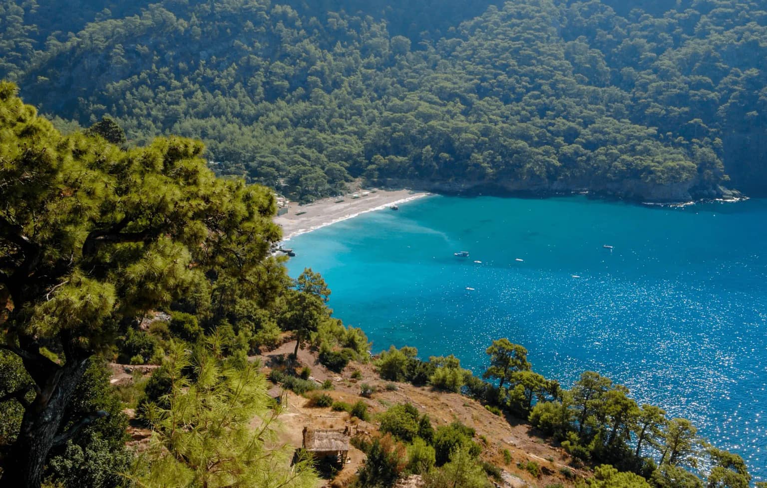 Travelers walking on the beach in Kabak Bay, with its turquoise sea surrounded by pine forests.