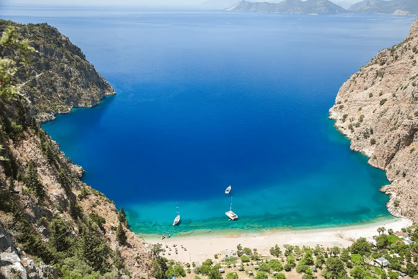 Travelers walking on the beach in Kabak Bay, with its turquoise sea surrounded by pine forests.