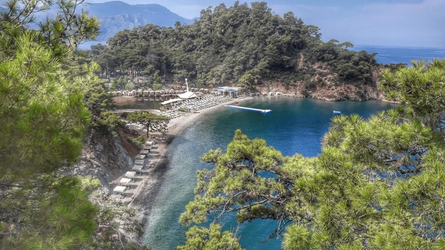 Boncuklu Koyu'nda, çam ağaçlarıyla çevrili sahile yakın demirlemiş birkaç küçük tekne.