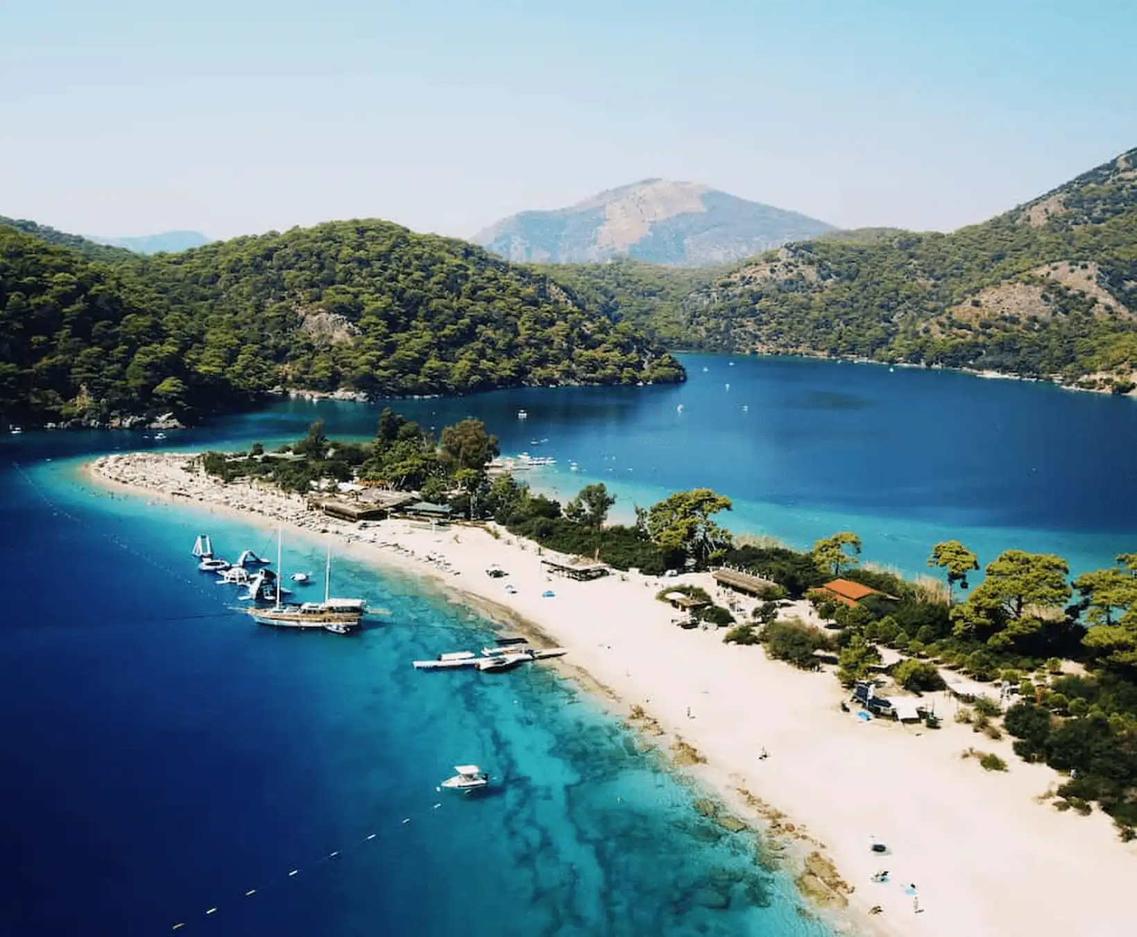 Eine Gulet und eine Segelyacht, die in einer von Pinienwäldern umgebenen türkisfarbenen Bucht in der Ägäis vor Anker liegen.